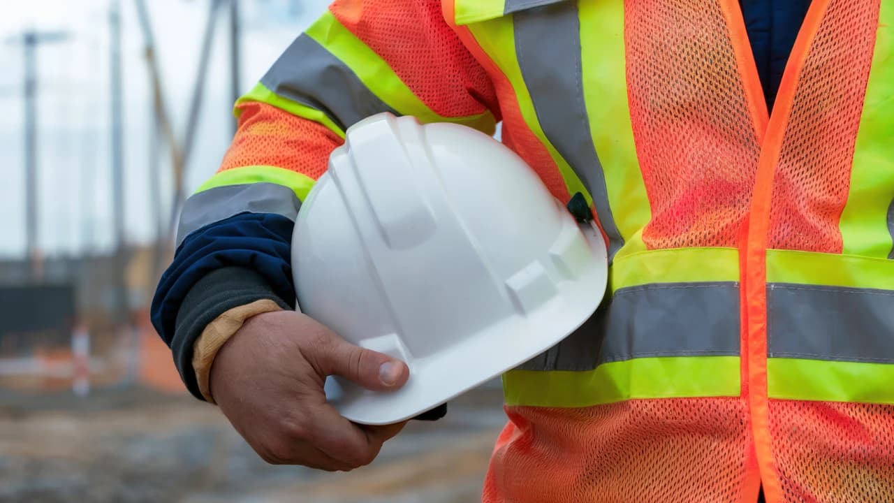 A construction worker in a high-visibility vest holding a hard hat on a job site