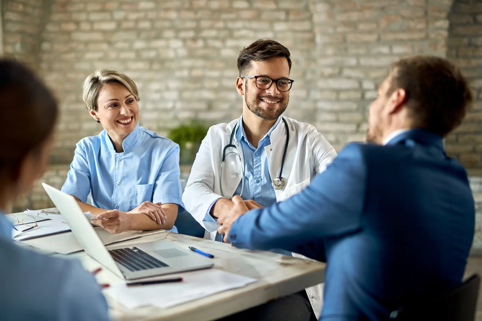Healthcare professionals meeting around a laptop, one of them smiling in a white coat with a stethoscope