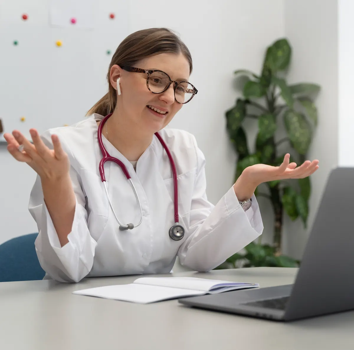 A doctor in a white coat talking to a colleague on a video call at her laptop