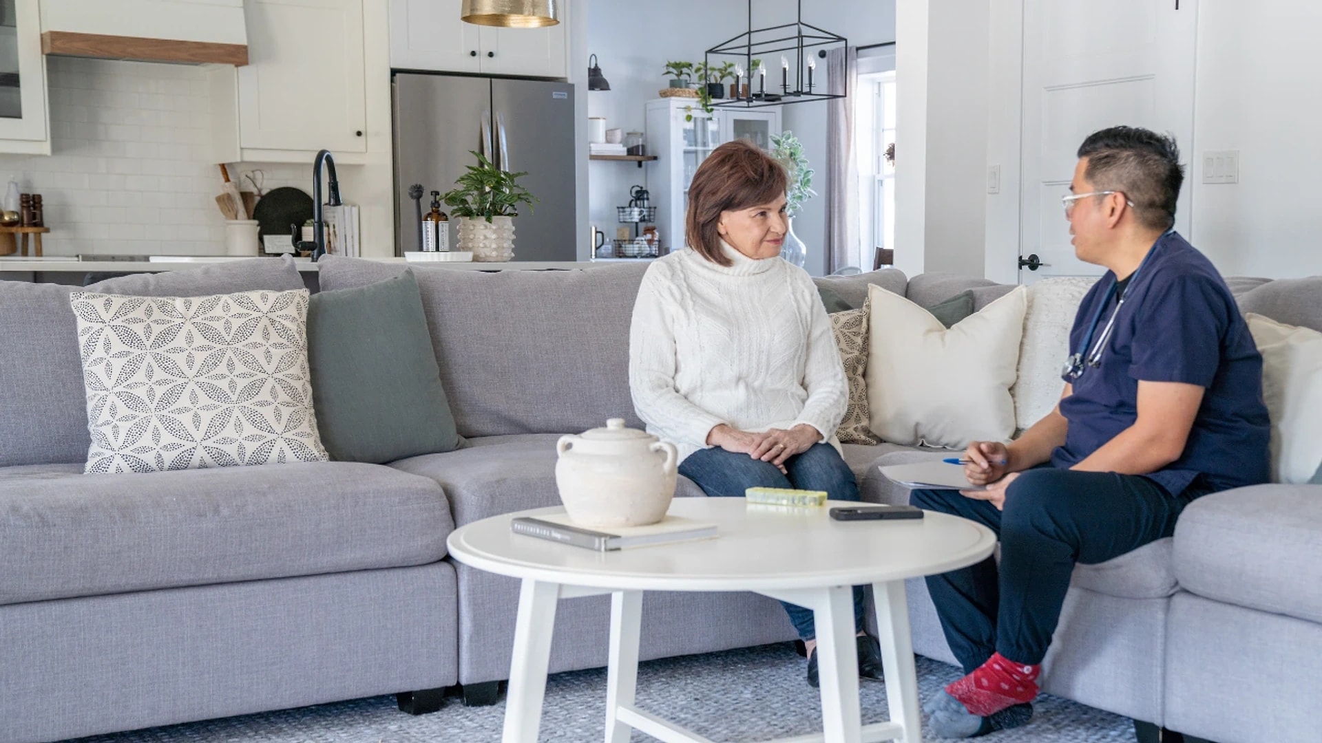 A home care nurse taking notes while talking with a client in her living room