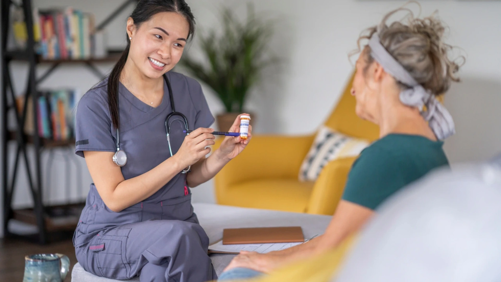 A caregiver explaining a prescription bottle to a client in her living room
