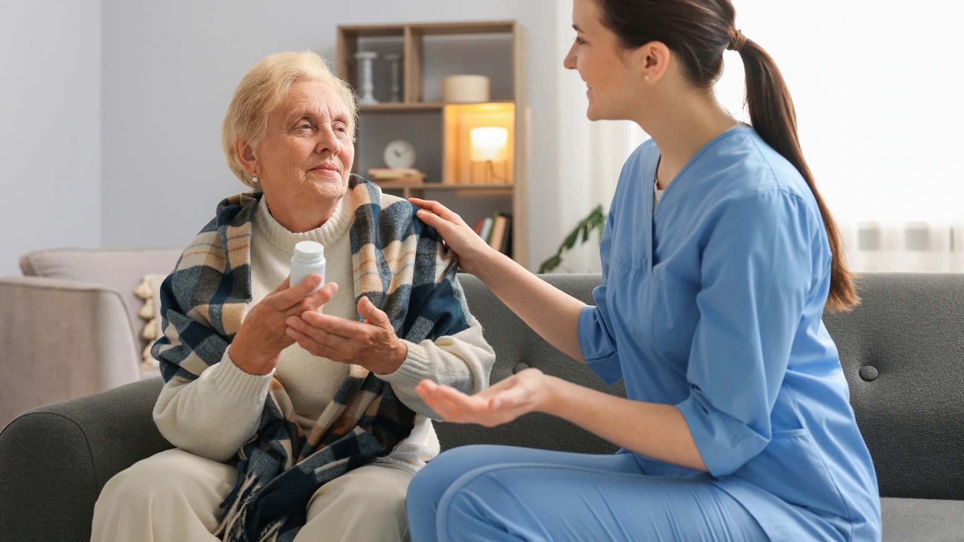 A home health nurse reassuring an older woman holding a medication bottle