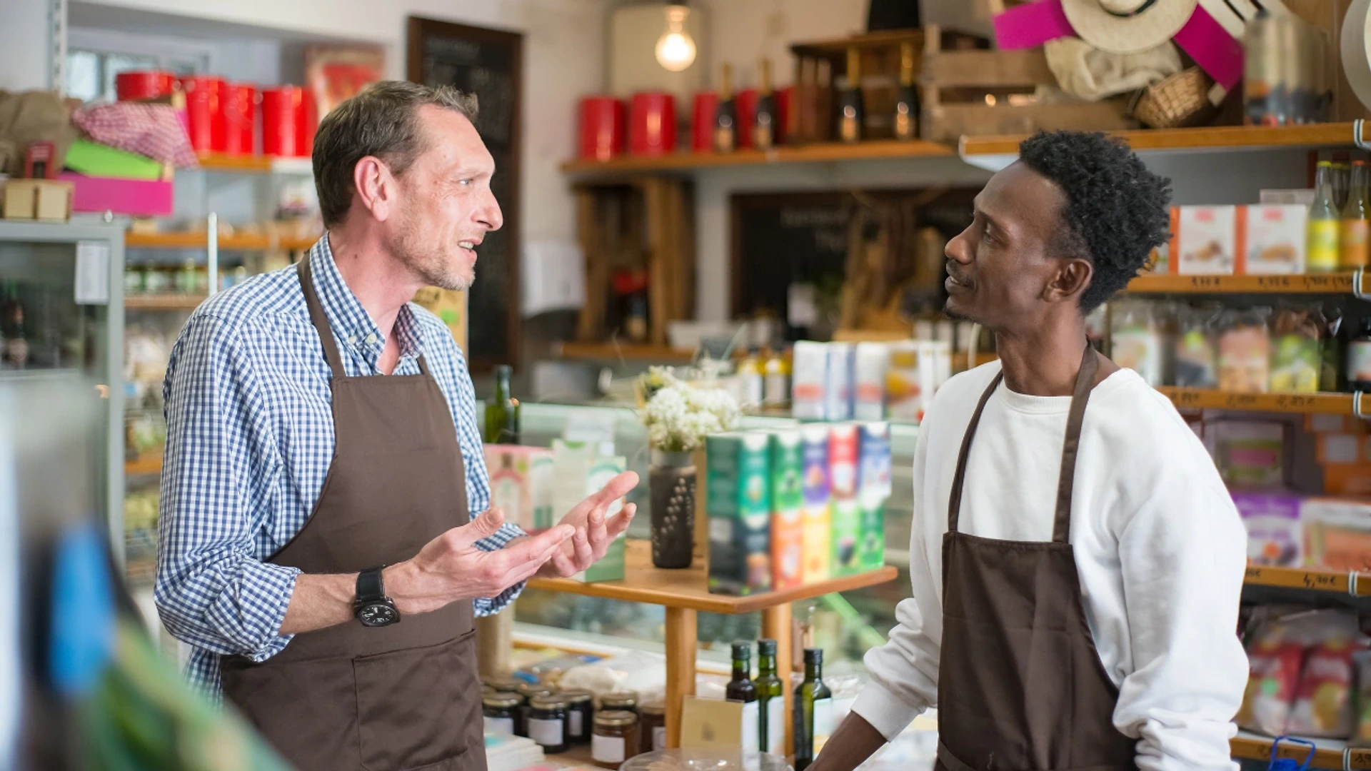 A store manager in an apron talking with a retail associate between shelves