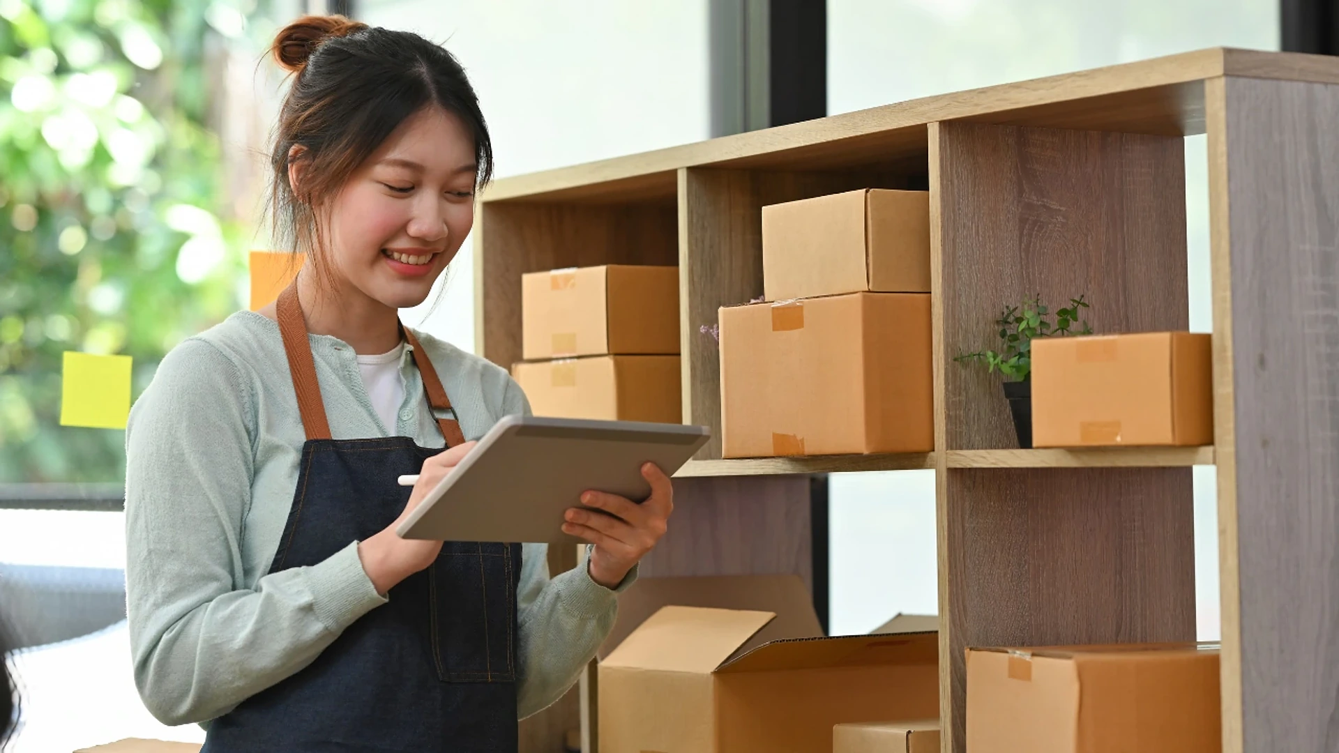 A smiling retail associate checking stock on a tablet beside shelves of boxes