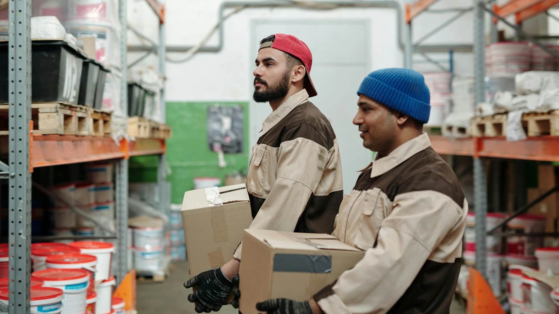 Two stockroom workers carrying boxes between warehouse shelves