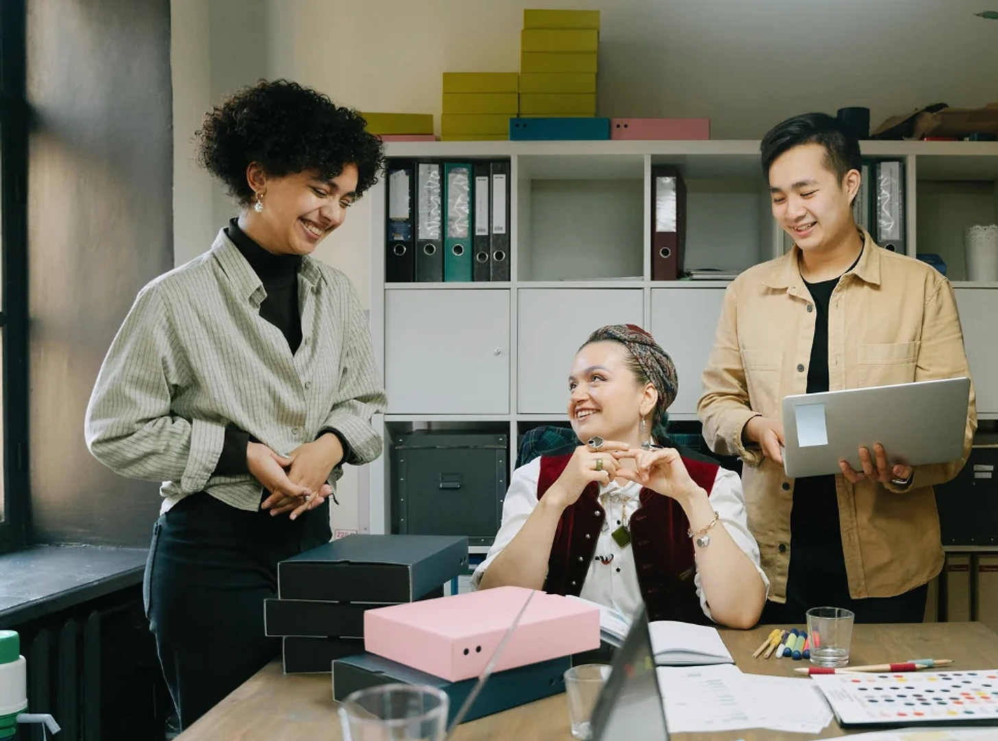 Colleagues talking beside a desk with a laptop and office files