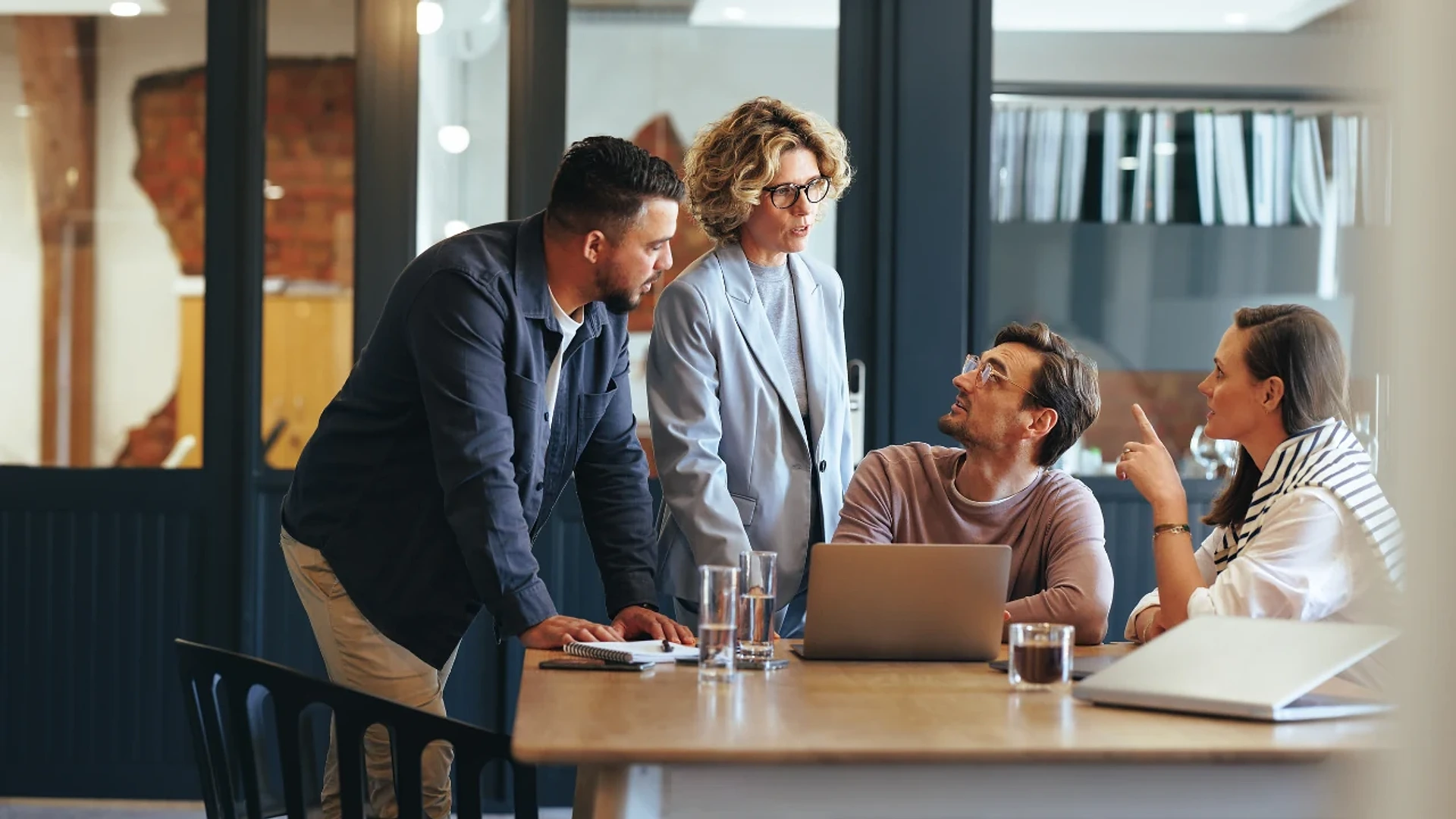 Four colleagues discussing work around a laptop in a meeting room