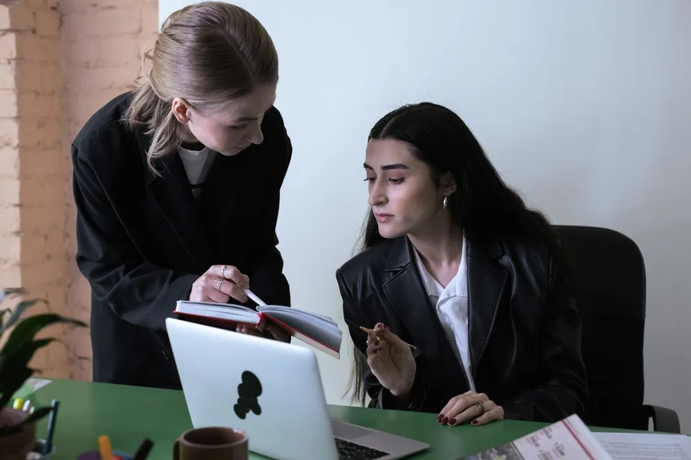 Two colleagues reviewing a schedule beside a laptop